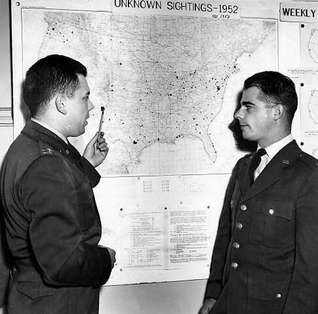 Black-and-white 1953 photograph of Captain Edward J. Ruppelt, left, standing beside another Air Force officer in front of a wall map.